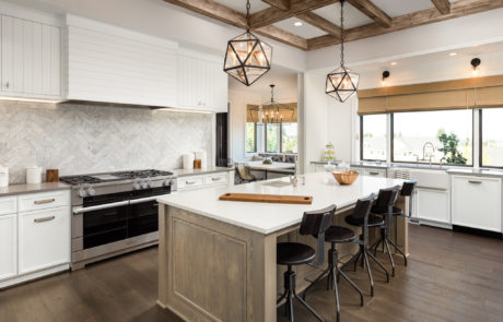 Kitchen Interior with Island, Sink, Cabinets, and Hardwood Floors in New Luxury Home. Includes elegant pendant light fixtures and wood beam ceiling